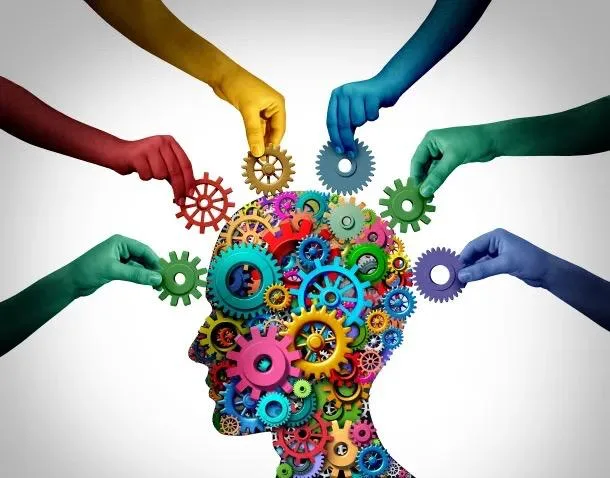 Many hands of different colours adding coloured gears to a head made of gears